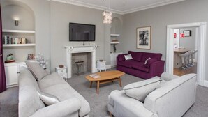 Una sala de estar con chimenea, televisor, sofá morado y una mesa de centro.
