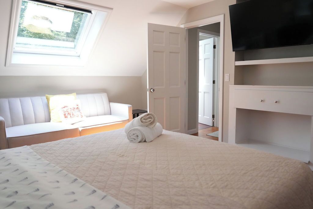 A bedroom with a bed, a white sofa, a TV, and a door leading to another room.