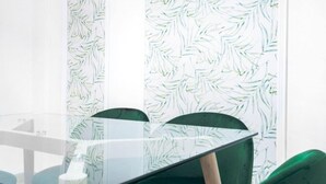 Une table avec un plateau en verre, des chaises, un papier peint à motifs et une fenêtre.