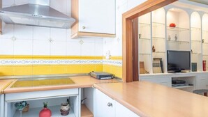 Une cuisine équipée d’une hotte en acier inoxydable, d’un plan de travail avec un grille-pain et d’un téléviseur posé sur une étagère d’un meuble.
