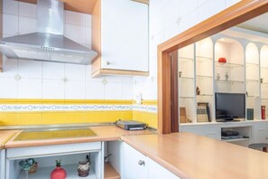 A kitchen with a stainless steel range hood, a countertop with a toaster, and a television on a cabinet shelf. - Stay near Feria, Madrid (Seville)