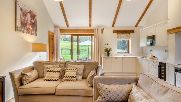 A living room with a sofa, a dining table, and a kitchen area with cabinets and a window. - 2 Bed in Bodmin (oc-m32909) (Saint Winnow)