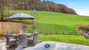 A hot tub with a wooden deck, wicker chairs, and a table with a glass. - 2 Bed in Bodmin (oc-w32907) (Saint Winnow)