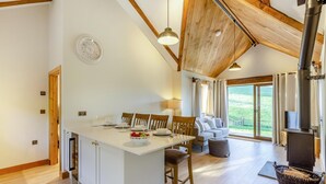 A modern kitchen with a central island, wooden beams, a large window, and a wood-burning stove. - 2 Bed in Bodmin (oc-w32907) (Saint Winnow)