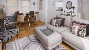 A living room with a sofa, a dining table, and chairs, a kitchen area, and a bathroom with a mirror and sink. - 2 Bed in Bath (oc-bhr50) (Bath)