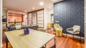 Ein modernes Wohnzimmer mit einem Esstisch, Sofas und einer Küchenzeile im Hintergrund.