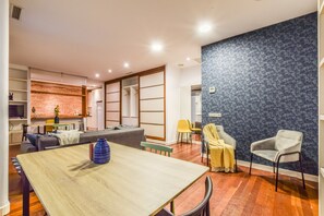 Ein modernes Wohnzimmer mit einem Esstisch, Sofas und einer Küchenzeile im Hintergrund.
