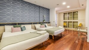 Ein Hotelzimmer mit zwei Betten, einem geometrischen Wanddesign, Holzböden und Blick auf einen Balkon mit Stühlen.
