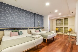 Ein Hotelzimmer mit zwei Betten, einem geometrischen Wanddesign, Holzböden und Blick auf einen Balkon mit Stühlen.
