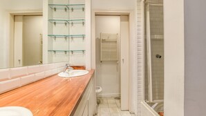 Ein Badezimmer mit Holzwaschtisch, Glasregal, Handtuchhalter, Dusche und Toilette.