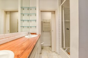 Ein Badezimmer mit Holzwaschtisch, Glasregal, Handtuchhalter, Dusche und Toilette.