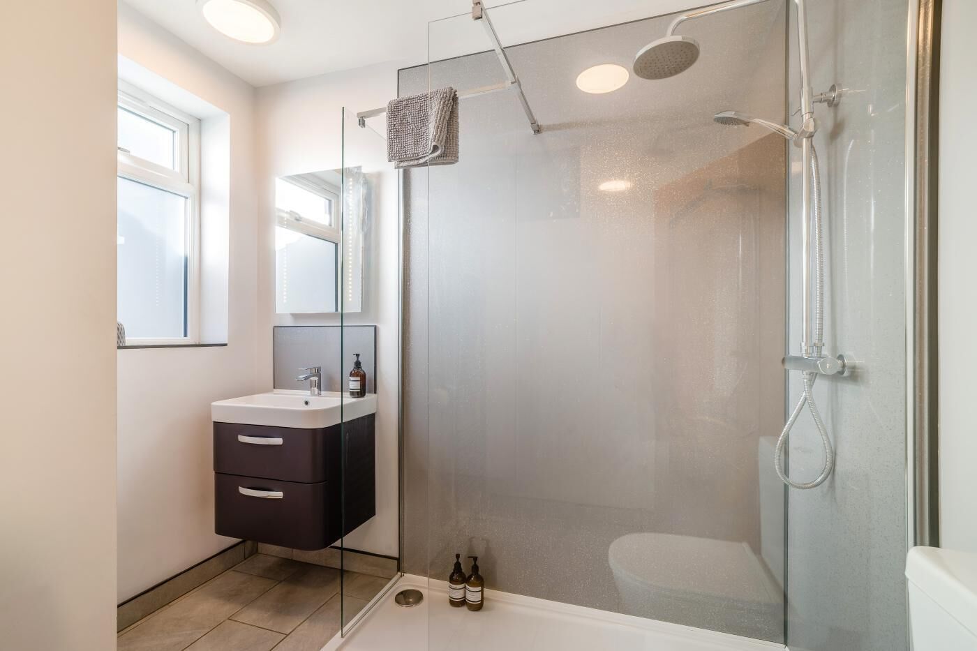 A modern bathroom with a glass-enclosed shower, a vanity with a mirror, and a window.