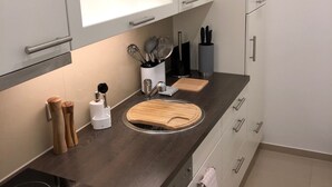 A modern kitchen with white cabinets, a black countertop, a wooden cutting board, and a built-in stove.