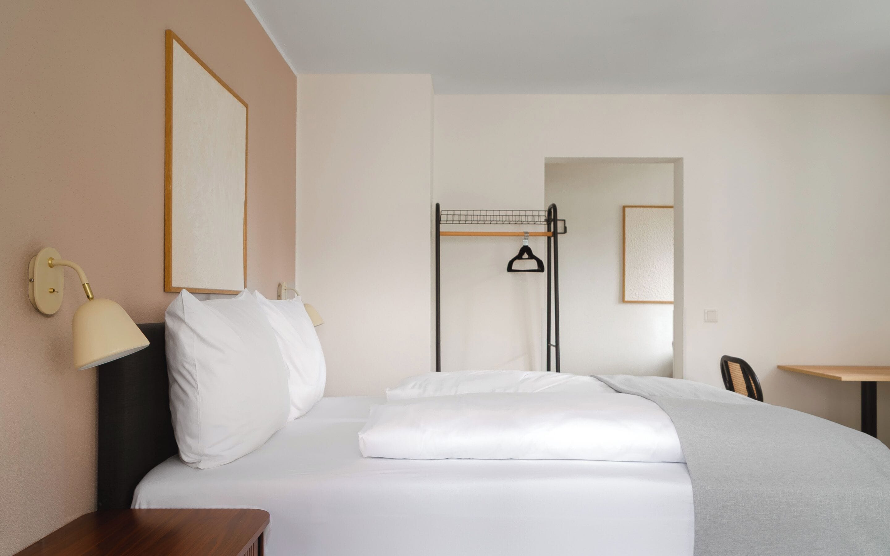 Une chambre d’hôtel comprenant un lit, une table de chevet, une lampe, un miroir et un porte-vêtements.