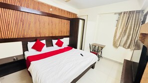 A hotel room with a wooden headboard, a bed with white bedding and red pillows, a bedside table, a chair, and a window with curtains. - Townhouse Star Square Vijay Nagar (Indore)