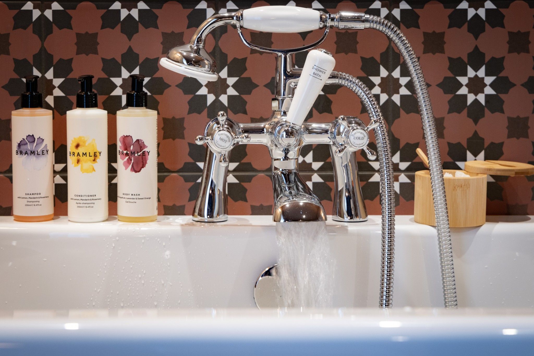 A bathroom with a modern shower, three bottles of Bramble body wash, and a patterned wall.