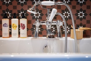 Un baño con ducha moderna, tres botellas de exfoliante corporal Bramble y una pared con diseño.
