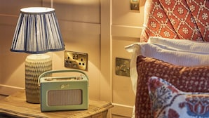 Een keurig opgemaakt slaapkamer met nachtkastje, lamp, radio en gestreepte kussens.