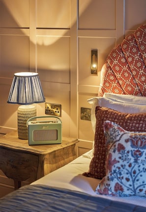 Un dormitorio ordenado con una mesita de noche, lámpara, radio y almohadones estampados.