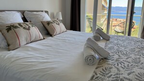 Habitación de hotel con cama, almohadas, una toalla enrollada y vistas al mar a través de amplias ventanas.