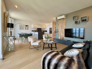 Ein modernes Wohnzimmer mit einer Couch, einem Fernseher und einem Essbereich mit Stühlen und einem Tisch.
