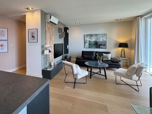 Un salon moderne doté d’un téléviseur à écran plat, d’un canapé, de deux fauteuils, d’une table basse et d’un coin repas avec une table en verre.