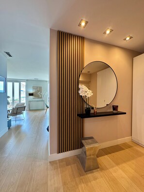 Un intérieur moderne avec un mur lambrissé en bois, un miroir rond, une petite étagère avec une bougie et une vue sur un coin repas.