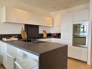 Une cuisine moderne avec des meubles blancs, un îlot central, des appareils en acier inoxydable et un pare-feu noir.