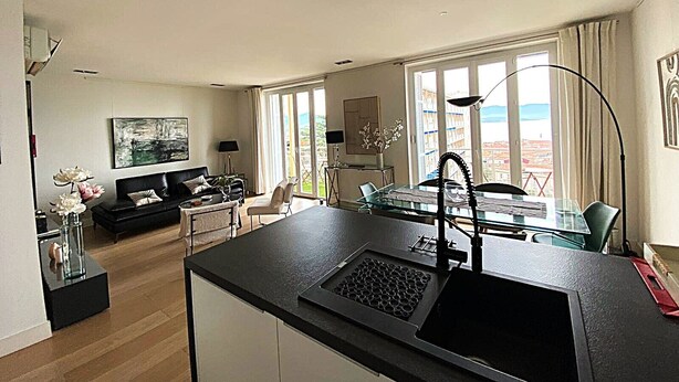 Una cocina moderna con una isla grande, un comedor con mesa de vidrio y una sala de estar con sofá y un cuadro.