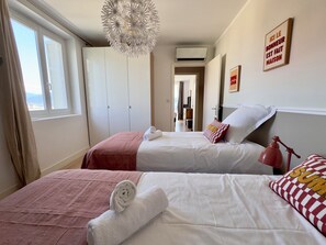 Et hotelværelse med to senge, en lysekrone, udsigt gennem vinduet og en dør til et andet rum.