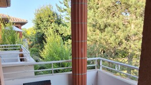 A balcony with a white railing, a wicker chair with a cushion, a small table, and a column.