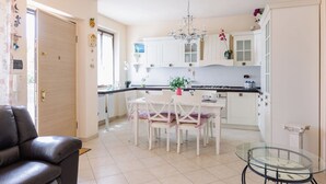 Une cuisine moderne avec des meubles blancs, une table à manger avec des chaises, une table basse en verre et un lustre.