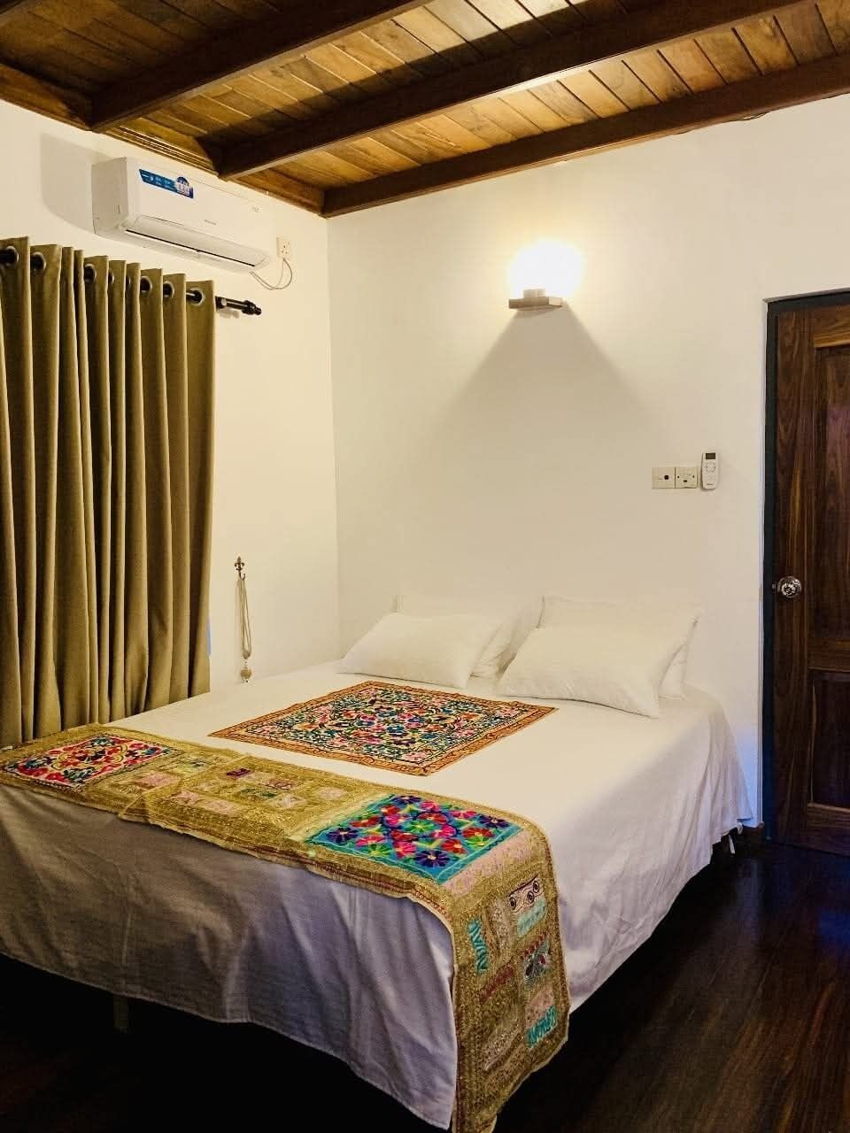 Een slaapkamer met een bed, een raam met gordijnen, een wandairconditioner en een deur.