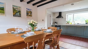 A dining area with a wooden table set for six, surrounded by chairs. A vase with flowers is on the table. - Araelfa (Llangollen)