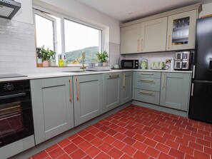 A kitchen with grey cabinets, a black refrigerator, and a red-tiled floor. - Araelfa (Llangollen)