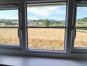 Ein Fenster mit Blick auf eine ländliche Landschaft, darunter Felder und Gebäude in der Ferne.