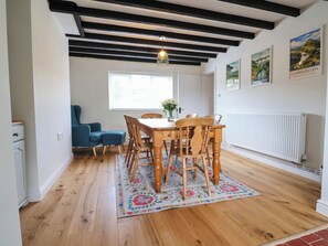 A dining area with a wooden table and chairs, a blue sofa, a floral rug, and a ceiling with exposed beams. - Araelfa (Llangollen)