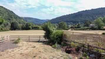 A fenced field with a view of a forested hill and a house in the distance.
