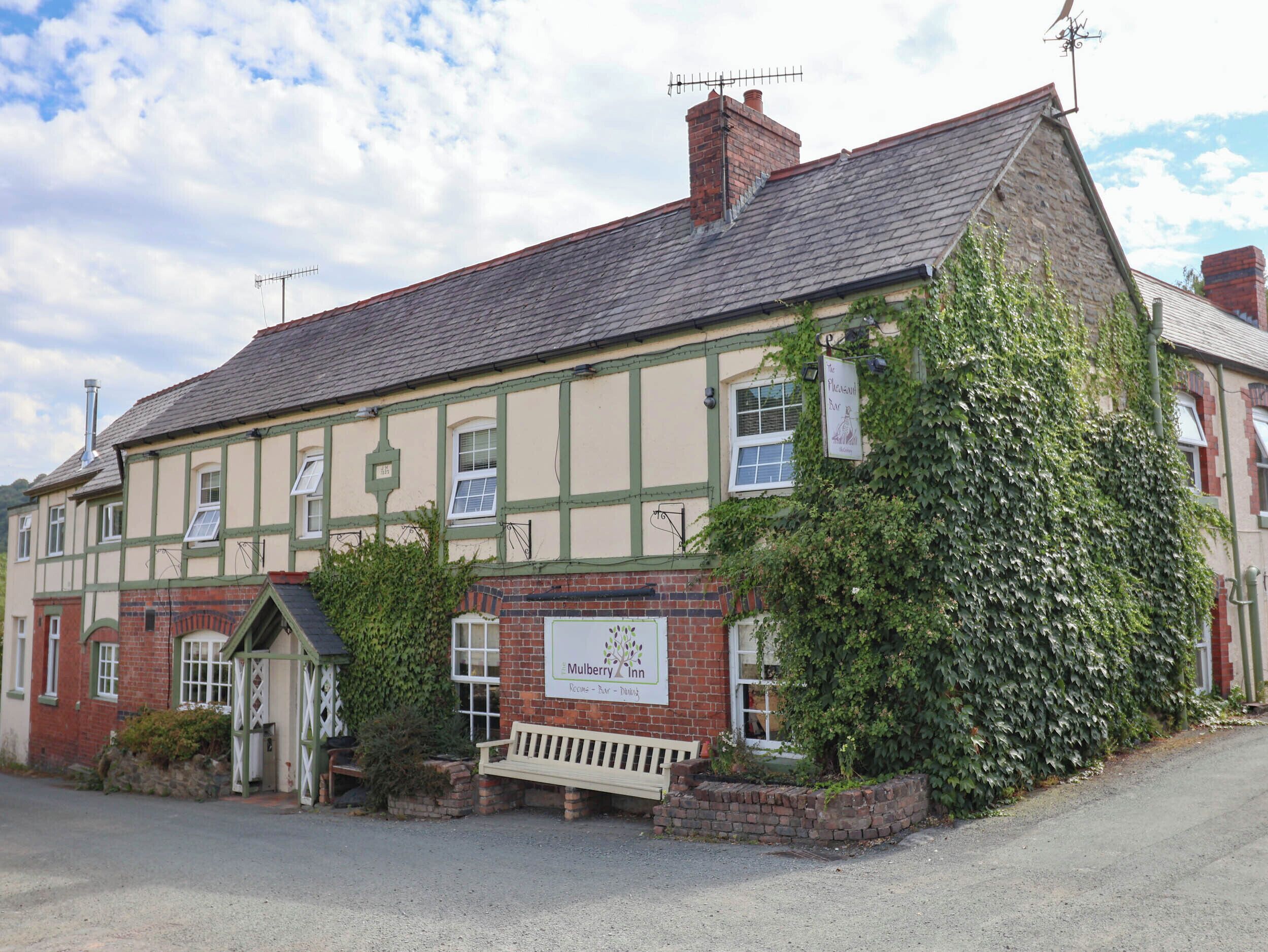 A traditional pub with a signboard, a bench outside, and a brick wall.