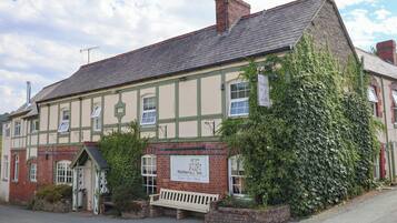 A traditional pub with a signboard, a bench outside, and a brick wall.