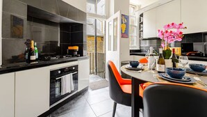 Ett modernt kök med svarta och vita skåp, en gasspis och en matplats med orange stolar och ett bord dukat för två personer.