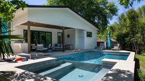 Ein modernes Haus mit Schwimmbad, Sitzgelegenheiten im Freien und einer überdachten Terrasse.