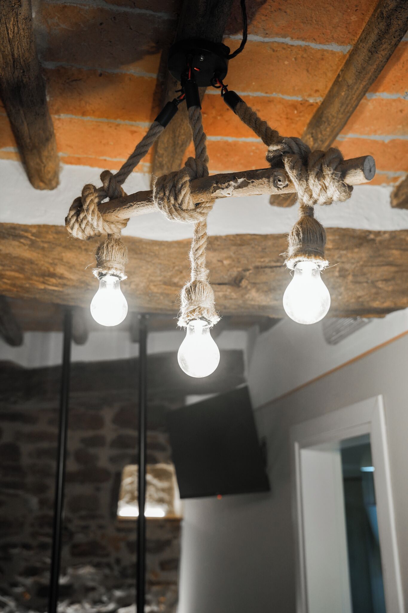 A rustic ceiling with exposed beams and a rope light fixture with two bulbs.