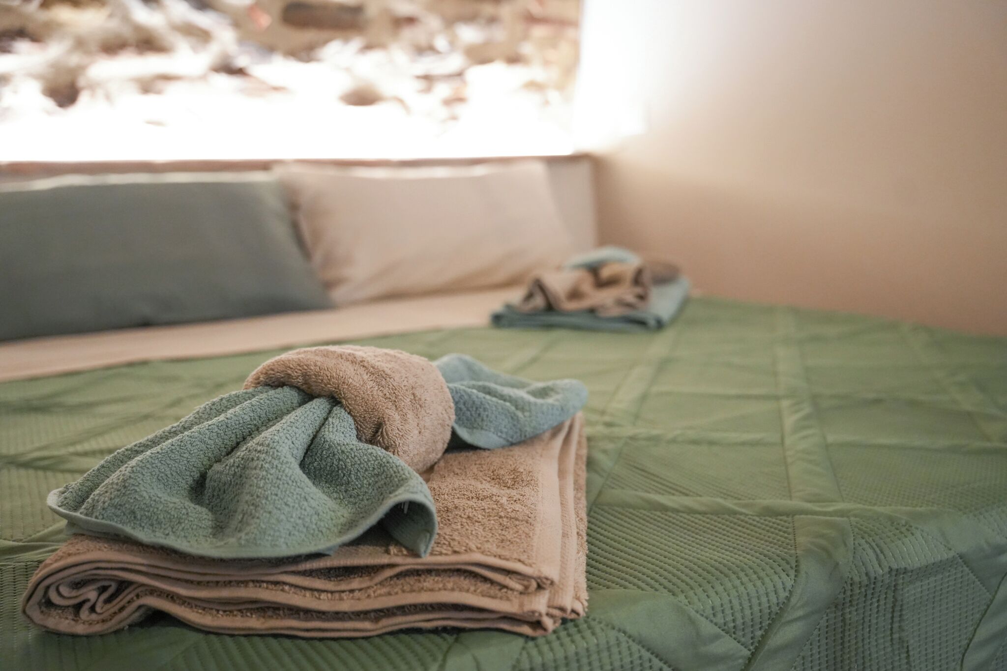 Ein Bett mit einer grünen Bettdecke, einem gefalteten Handtuch und einem Kopfkissen.