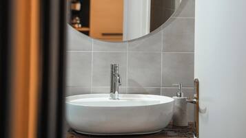 A bathroom with a round mirror, white sink, and wooden countertop.