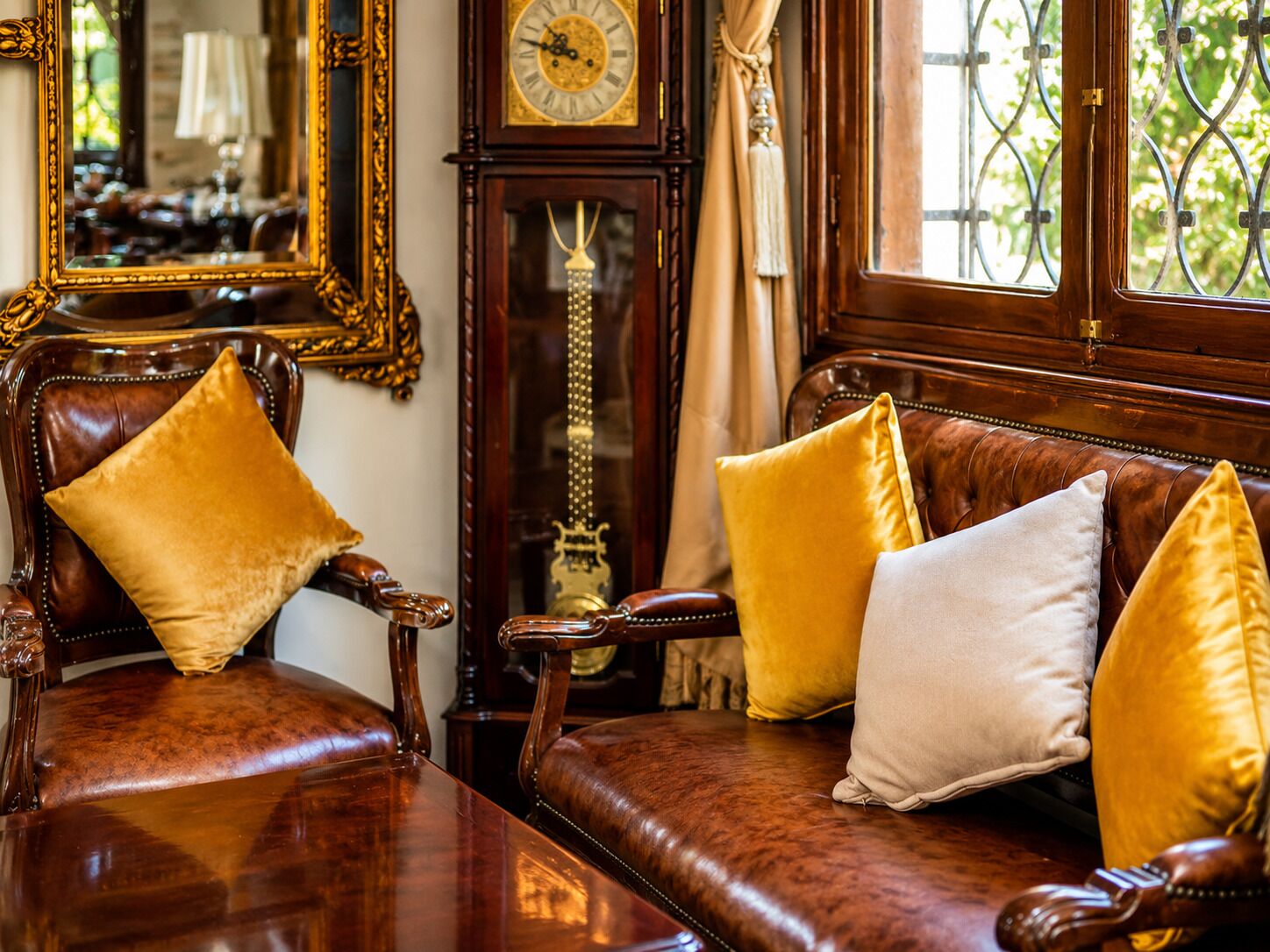 A room with a wooden sofa, two armchairs, a wooden table, a large mirror, and a wall clock.