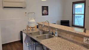 Uma cozinha com bancadas de granito, pias de aço inoxidável, ar condicionado embutido, iluminação pendente e uma janela com vista.