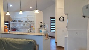 Uma cozinha moderna com iluminação pendente, uma área de jantar com mesa de vidro, um sofá e um banco de madeira.