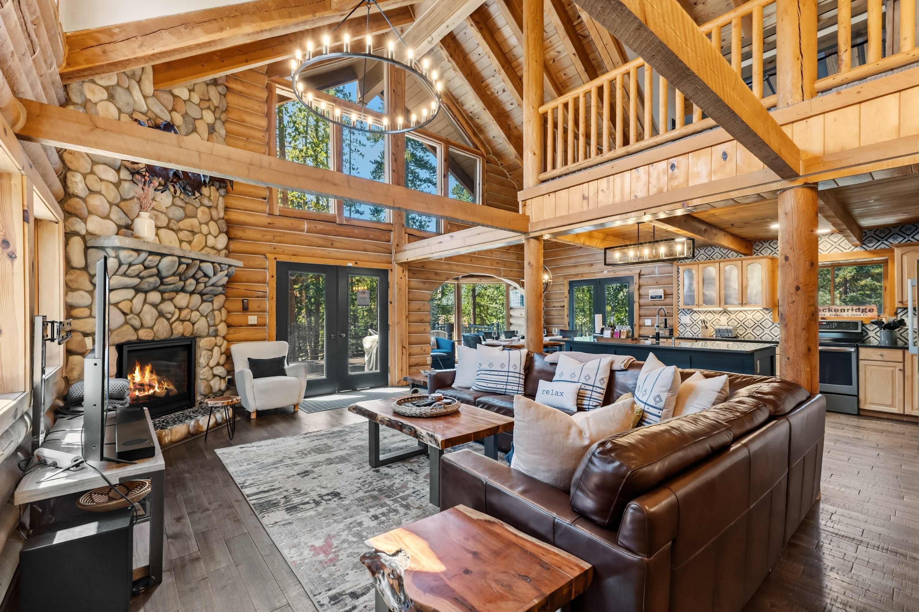 A spacious log cabin interior with a fireplace, leather sofa, and a dining area.