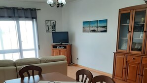 Un'area pranzo con tavolo imbandito per quattro persone, una poltrona, un televisore e un mobile.